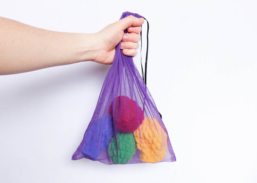 A hand holding a purple mesh drying bag containing four EcoSplat reusable water balloons of different colours: red, yellow, blue, green